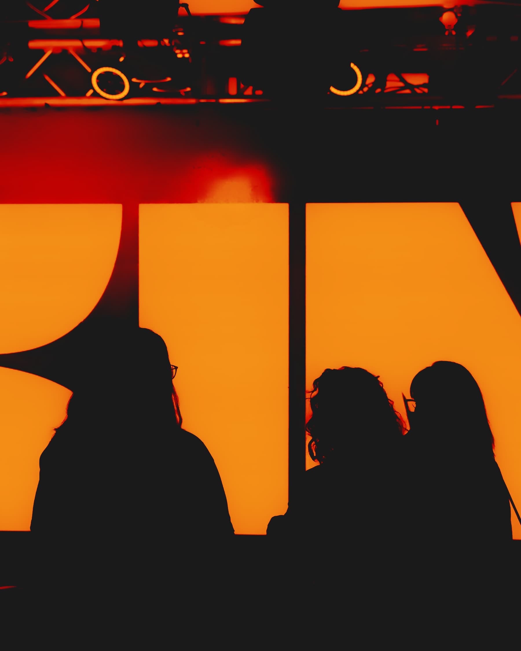 Orange-lit silhouettes of three people against a backlit Kin sign