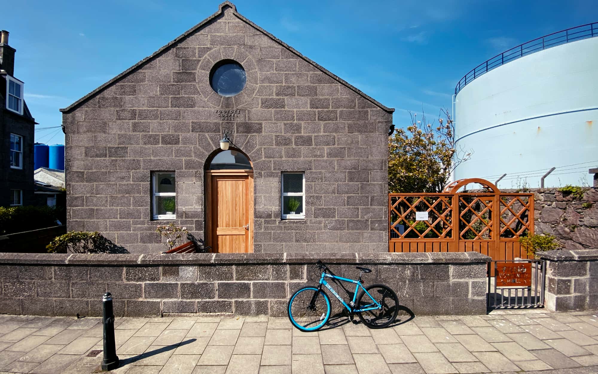 Fittie Community Hall, a granite former gospel hall with an arched wooden door, under blue sky.