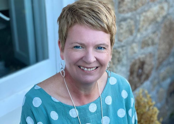 The photo shows Edel Harris OBE. She has a short, styled haircut and is smiling warmly at the camera. She’s wearing a teal to