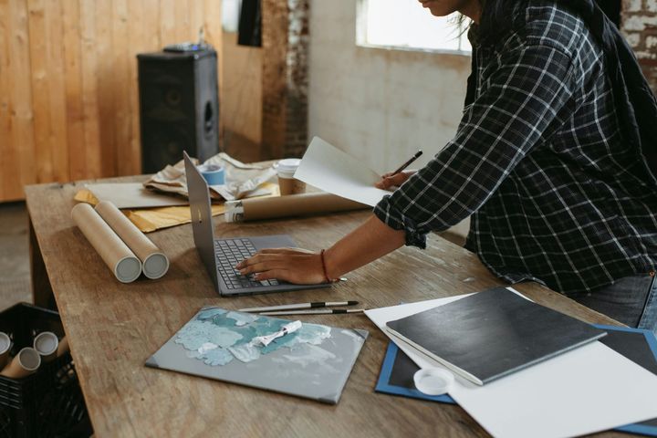 Person working on a laptop beside notes and art supplies