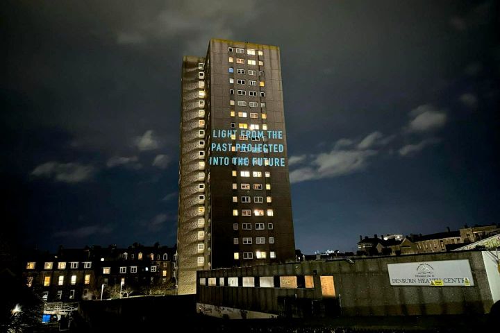 Tower block at night with illuminated windows and blue text projected onto its facade.