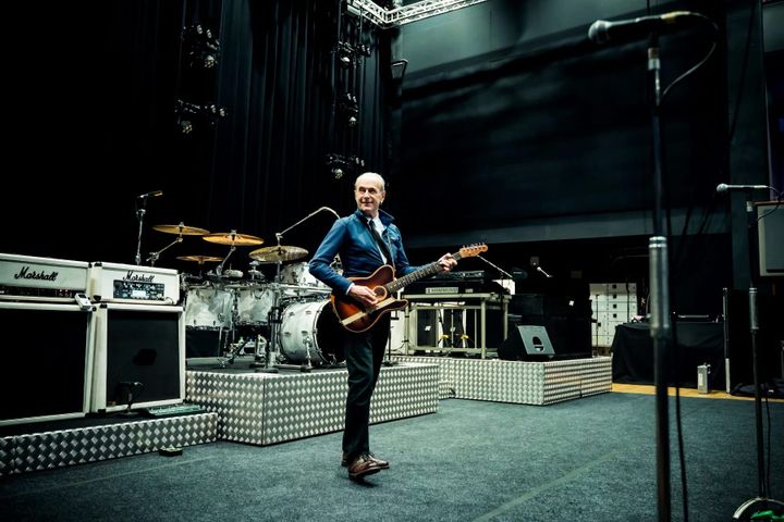 Francis Rossi on stage with a guitar, surrounded by drums, amps and mics during soundcheck