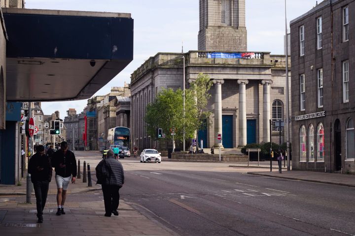A photo of King Street in Aberdeen featuring granite buildings, including the neoclassical Aberdeen Arts Centre with its imposing pillars and blue doors. Vehicles and pedestrians are visible.