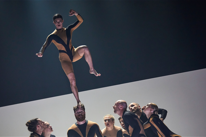 Performer balances on another’s head during Circa’s acrobatic show Wolf, with cast looking on.