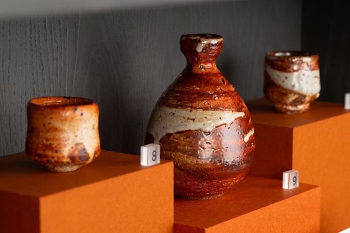 Three rustic glazed pots with reddish-brown and cream swirls displayed on orange plinths.