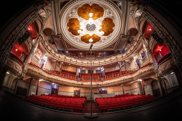 View from The Tivoli stage showing ornate ceiling, red seats and microphone centre stage.