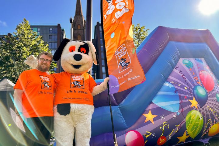 Charlie Dog mascot and volunteer in orange Charlie House t-shirts beside inflatable at Big Bounce event.