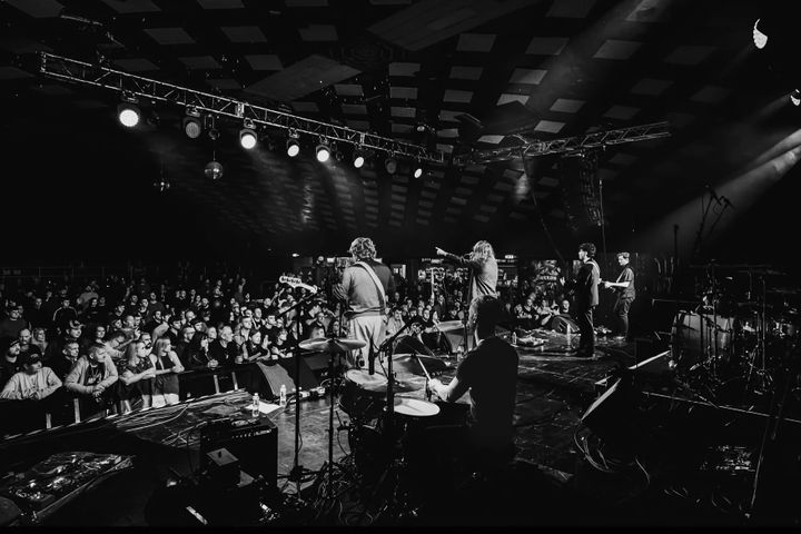 The Capollos perform live in a packed venue, captured in black and white from behind the drummer.
