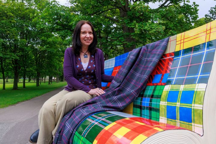 Sandra Russell sits on a painted bench shaped like an open book, covered in colourful tartan patterns.