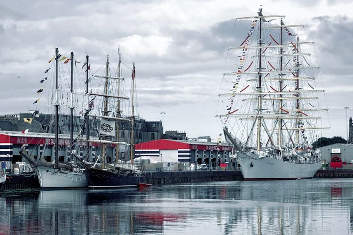Tall ships docked in Aberdeen Harbour, sails down and masts lined with colourful signal flags.