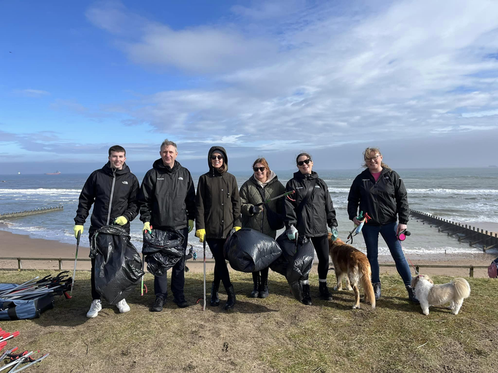 Six people and two dogs standing with litter pickers and bin bags on a beachside path.