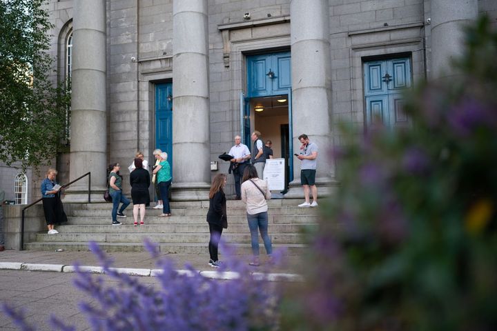 People on steps outside Aberdeen Arts Centre before a show, with purple flowers in foreground.