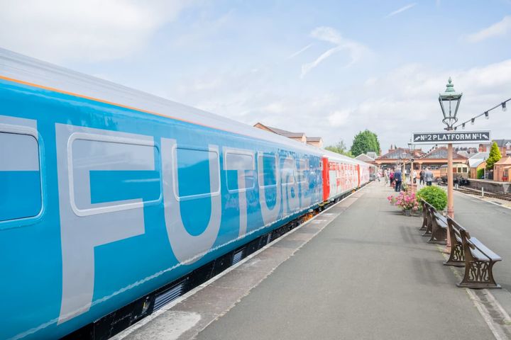 Bright blue train carriage with "FUTURE" written in large white letters, stationed at Platform of a heritage railway station.