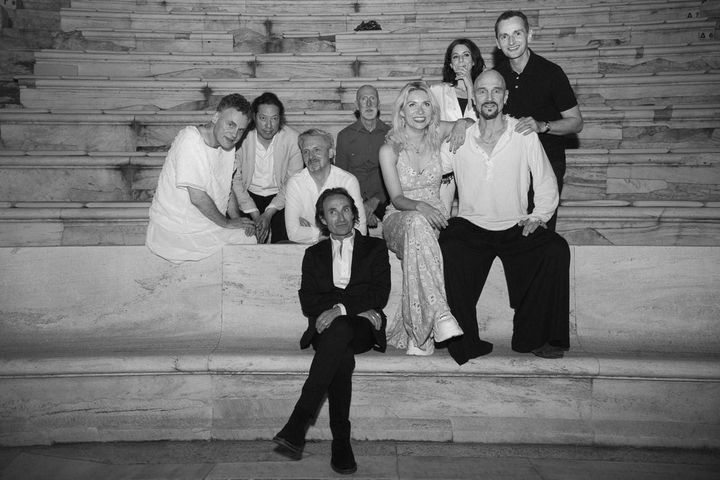 Black and white photograph of band members posed on wooden steps, with one member seated at the front and the others arranged on ascending levels behind them.