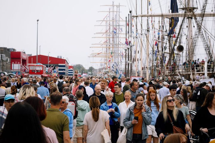 Crowds walking along Aberdeen harbour with tall ships and masts visible in background