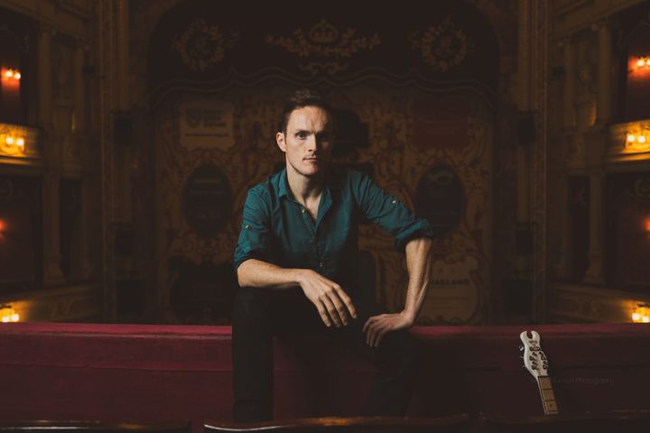 Oliver Richard seated at His Majesty's Theatre with guitar beside him