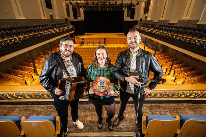 Tomàs Callister, Ellie Beaton and Paddy Callaghan at Music Hall holding accordion, awards sign and fiddle.
