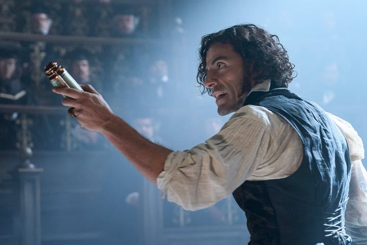 Oscar Isaac in period costume with curly dark hair holding brass electrical instrument aloft with intense expression
