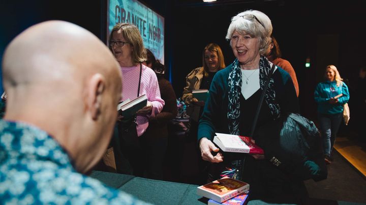 Readers queue with books at an author signing table at Granite Noir.