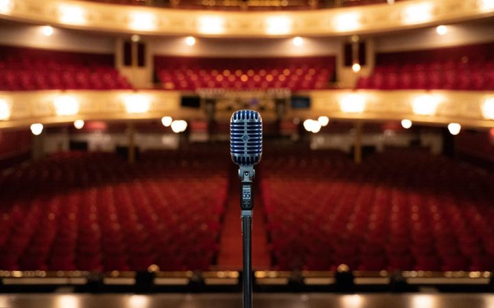 A vintage microphone on stage at His Majesty's Theatre, with the empty red-seated auditorium behind.