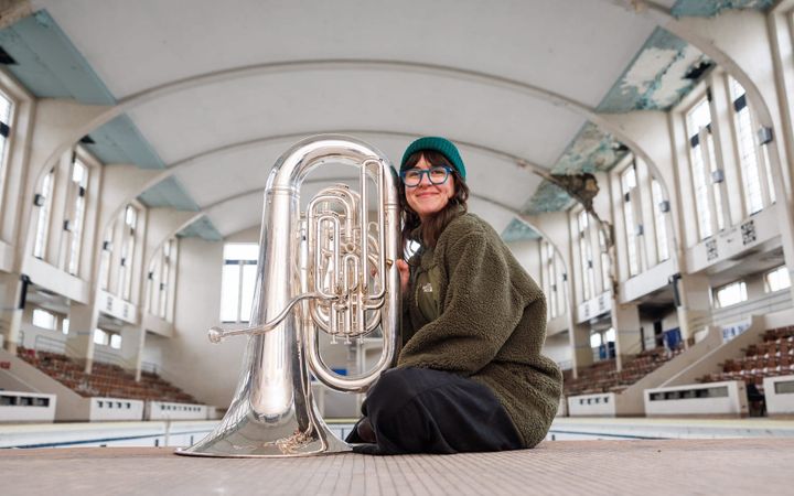 Danielle Price kneels with her tuba on the tiled floor of Bon Accord Baths' empty Art Deco pool hall.