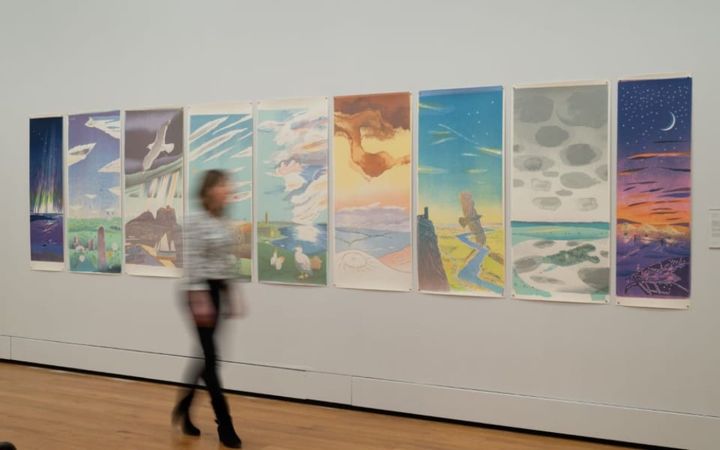 A visitor walks past a row of nine large colourful prints at Aberdeen Art Gallery.