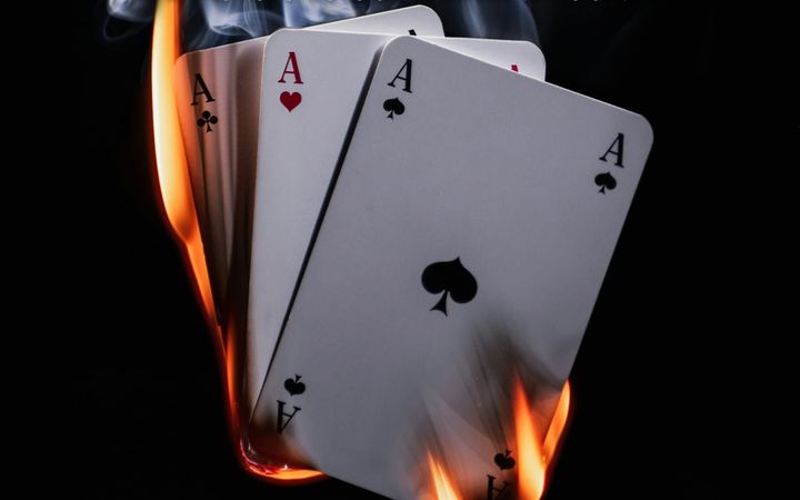 Four aces fanned out and engulfed in flames against a black background