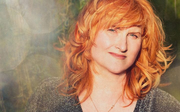 Eddi Reader, red-haired woman in a sparkly top, smiling softly against a blurred green background