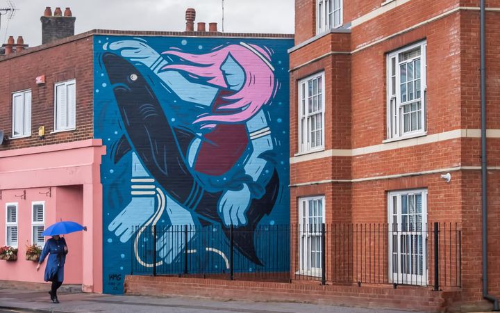 KMG mural depicting a pink-haired figure holding a shark, painted on a brick wall