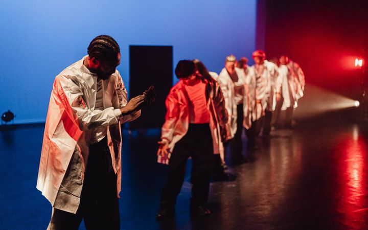 THREE60 dancers in white coats perform on stage under blue and red lighting