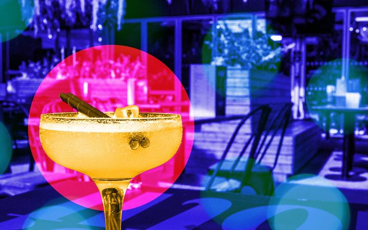 Salt-rimmed cocktail with lemon twist on turquoise-patterned surface, outdoor bar seating behind.