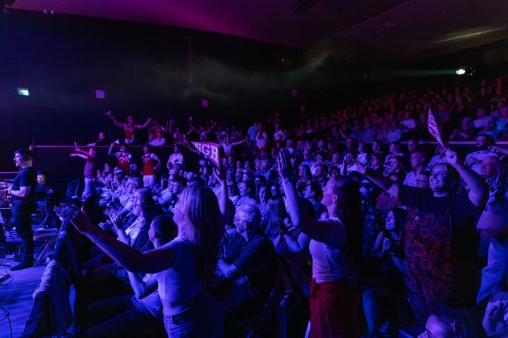 A packed audience cheers under purple stage lighting at Aberdeen Arts Centre
