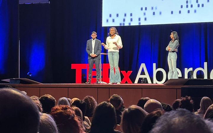 Three speakers on stage at TEDxAberdeen with the audience in the foreground