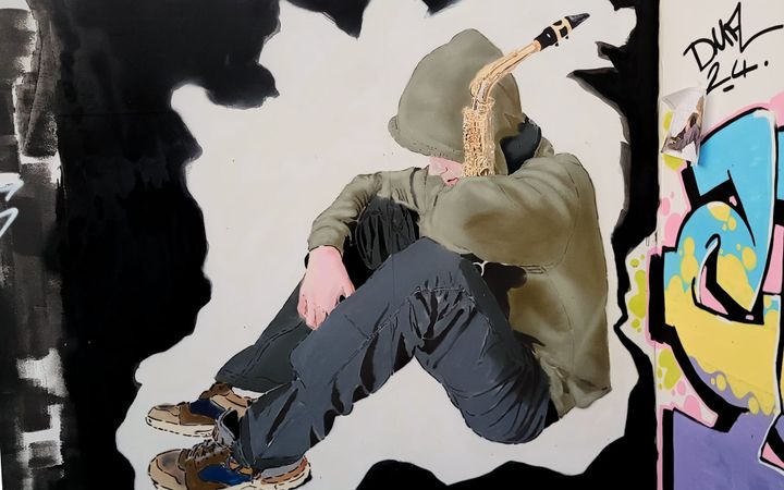 Stencil mural of a hooded figure seated on the ground playing a saxophone