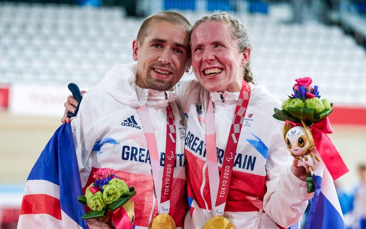 Neil Fachie and Lora Fachie embrace, gold medals round their necks and draped in a union jack flag.