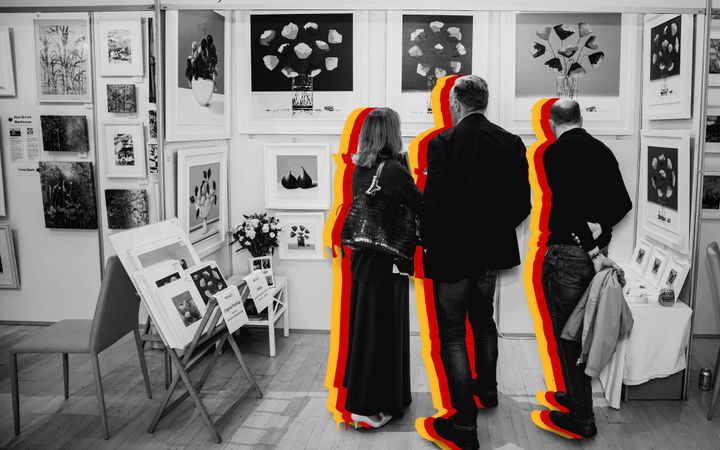 Three visitors viewed from behind, browsing framed prints on a gallery wall, in silhouette.