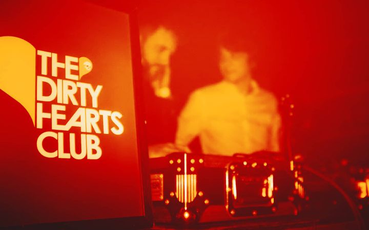 The Dirty Hearts Club sign lit up red beside a DJ silhouetted at the decks
