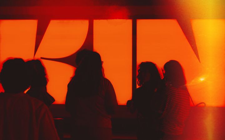 Silhouetted figures stand before a glowing orange screen showing the Kin logo.