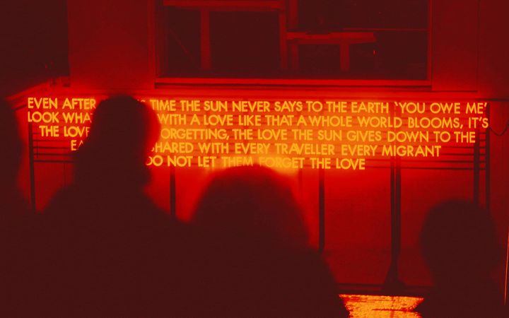 Robert Montgomery's illuminated poem glows red at Bon Accord Baths, silhouettes watching below