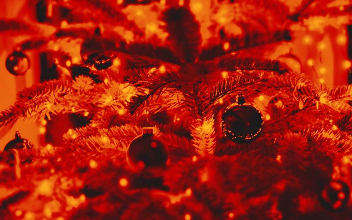 Close-up of Christmas tree branches with dark baubles and warm fairy lights