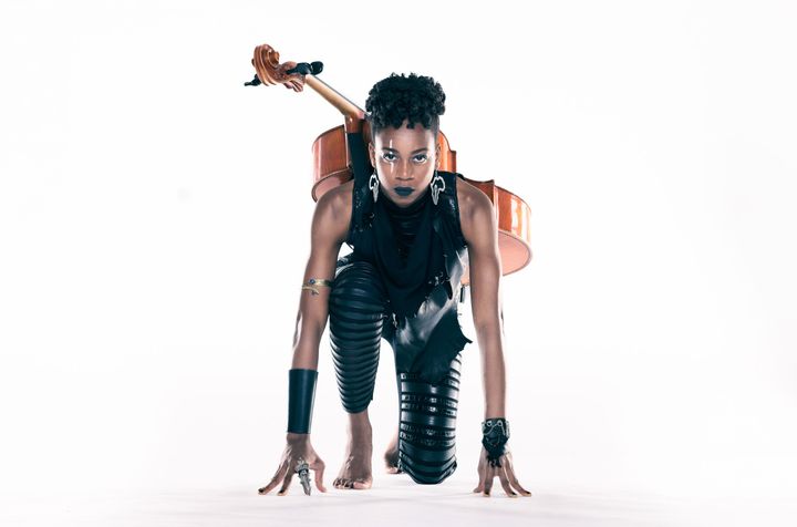 An athletic Ayanna Witter-Johnson on her knees like she was at the start of a race. She has her cello strapped to her back.