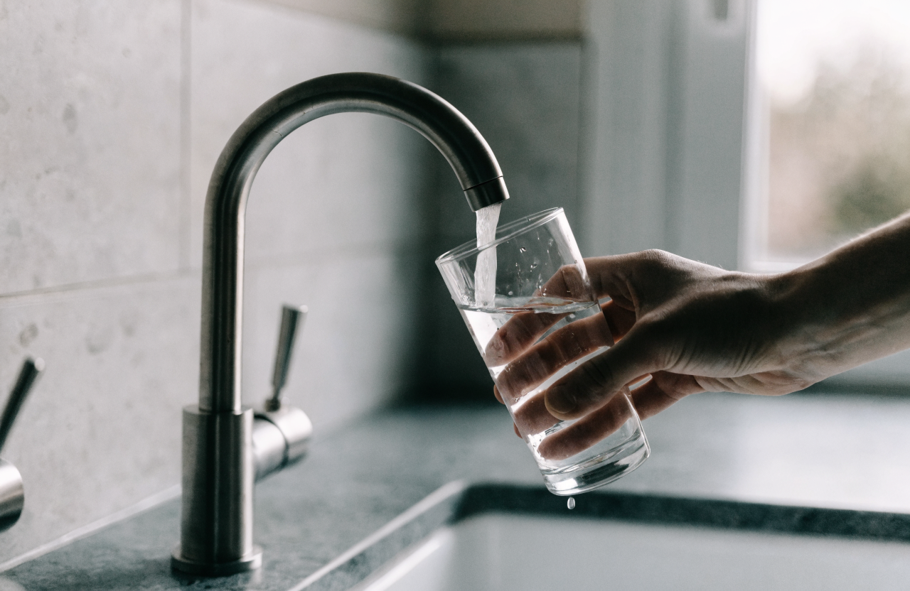 A hand fills a glass from a kitchen tap in soft window light.
