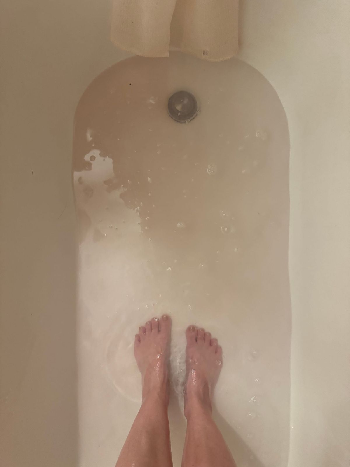 a photo taken in the bath of my feet as the water, tinged with blood to a very light pink, drains away.