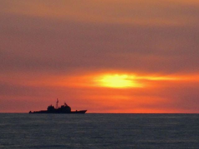 A ship on the horizon steaming toward the sunset.
