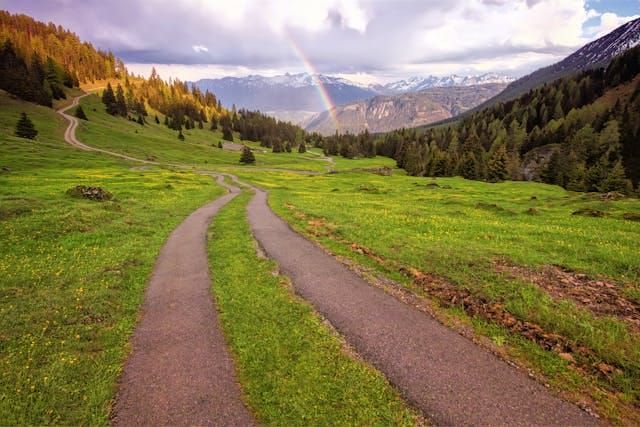 A path leading up into the mountains with a rainbow in the distance.