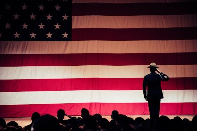 Drill sergeant standing on stage saluting an American flag.