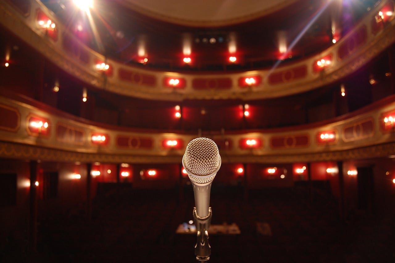 A photo of a theater, viewed from the stage looking out to the audience, with a microphone facing the viewer.