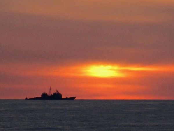 A ship on the horizon steaming toward the sunset.