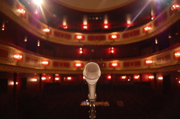 A photo of a theater, viewed from the stage looking out to the audience, with a microphone facing the viewer.