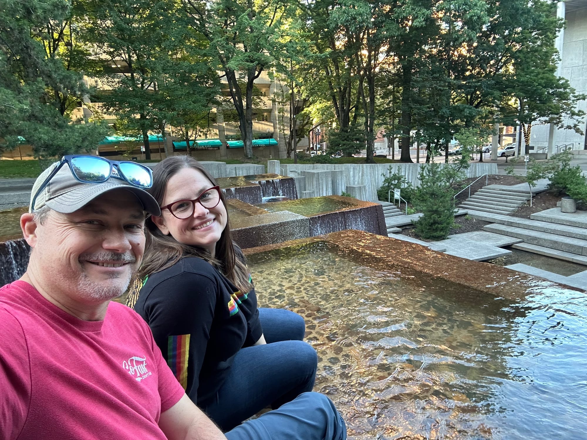 Two people sit smiling beside the cascading concrete foun